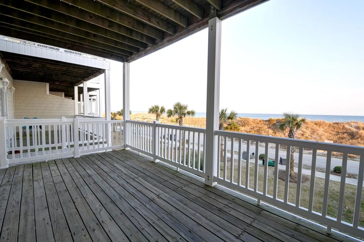This exterior image features a wooden deck overlooking the ocean, surrounded by palm trees. The serene setting suggests a perfect spot for relaxing outdoors, with clear views of the water and sky, ideal for enjoying time with pets while remaining close to nature.