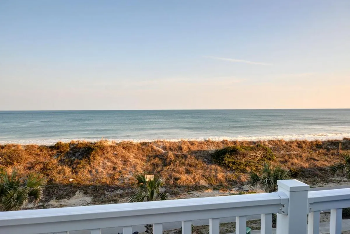 A sweeping view of the ocean framed by lush dune vegetation, stretching out to a tranquil horizon. The inviting scene encourages guests to stroll along the shore, watch the waves, and enjoy the sunset.