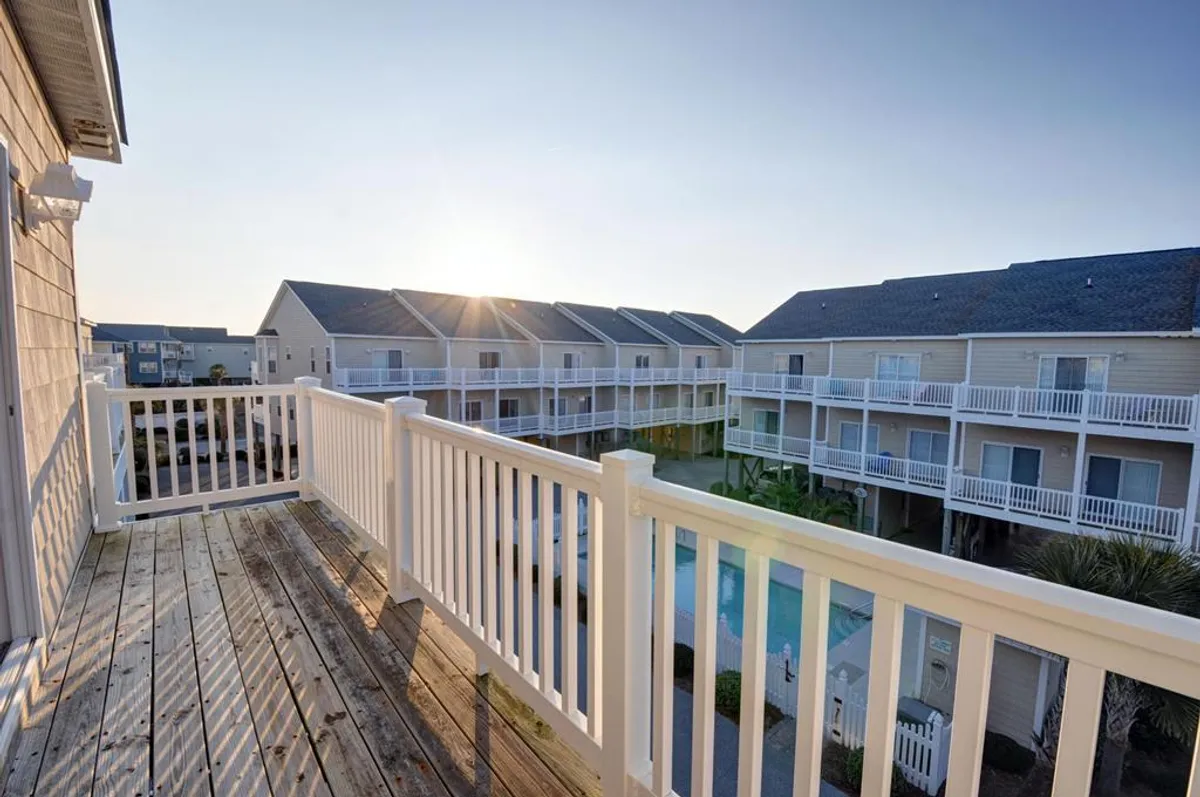 A serene exterior view from a balcony overlooking the community pool, neighboring buildings, and a glowing sunset sky. The pool area is inviting, while the balcony sets the scene for gathering and relaxing as a family in the evenings.