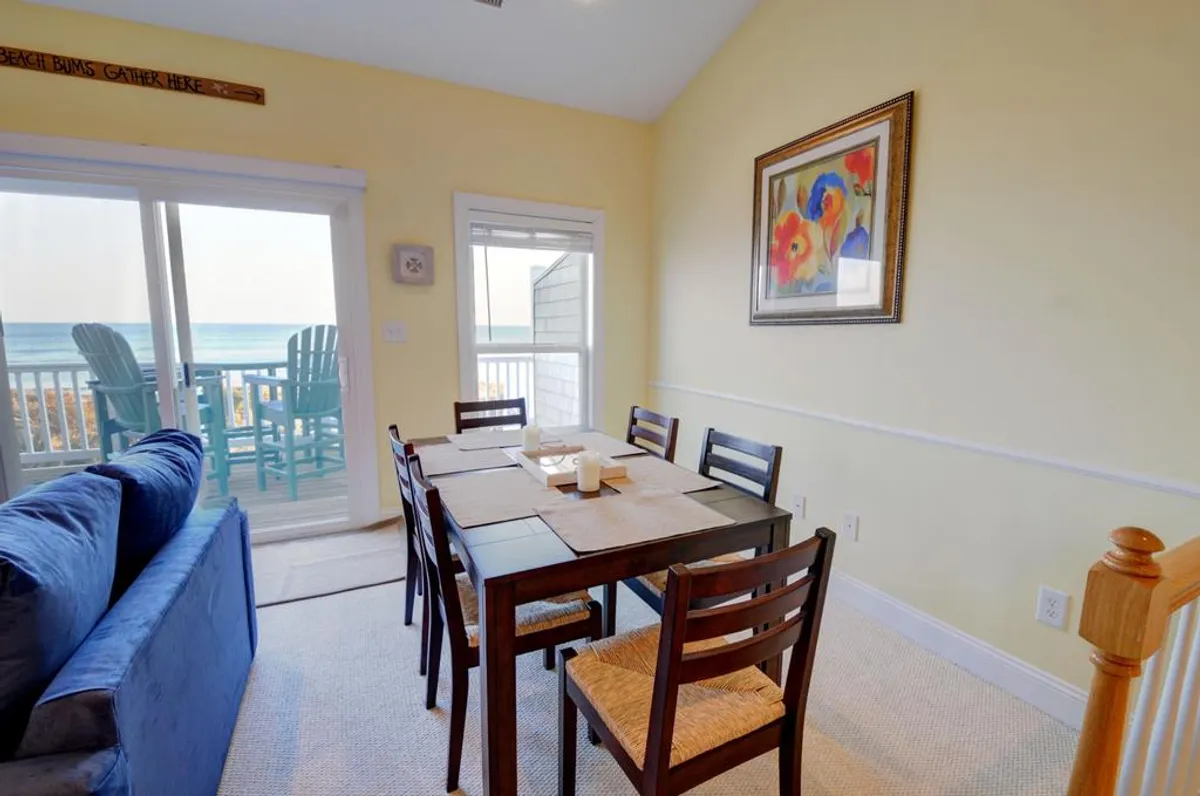 A dining area featuring a modern table set before large windows framing a sweeping ocean view. Artwork on the wall adds personality, and the scene is bathed in cheerful natural light—perfect for sunrise breakfasts or celebration dinners with the sound of waves nearby.