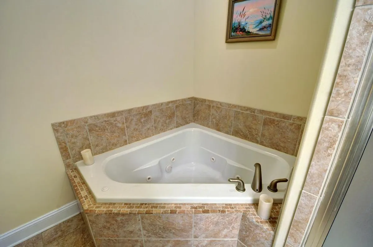 This image features a tranquil interior bathroom setting with a jacuzzi tub, surrounded by tasteful decorative artwork and stylish tilework. The atmosphere is serene, evoking the relaxing, spa-like experience of soaking in the jacuzzi with a glass of wine in hand.