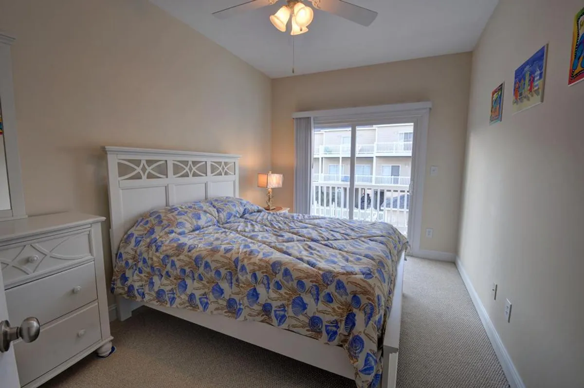 This image features a tranquil bedroom with a bed adorned in colorful bedding, a sunlit window, and a nightstand topped with a lamp. The atmosphere is both inviting and serene, ideal for relaxation after a day at the beach.
