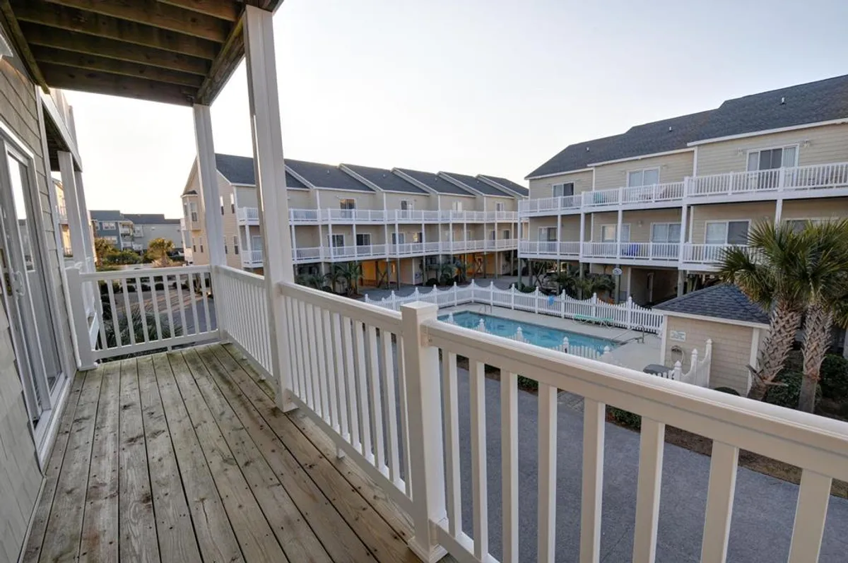 Taken from a balcony, this image overlooks the pool area and surrounding buildings with palm trees gently swaying. It suggests a tranquil and inviting space for morning coffee, sunset watching, or gathering with friends.